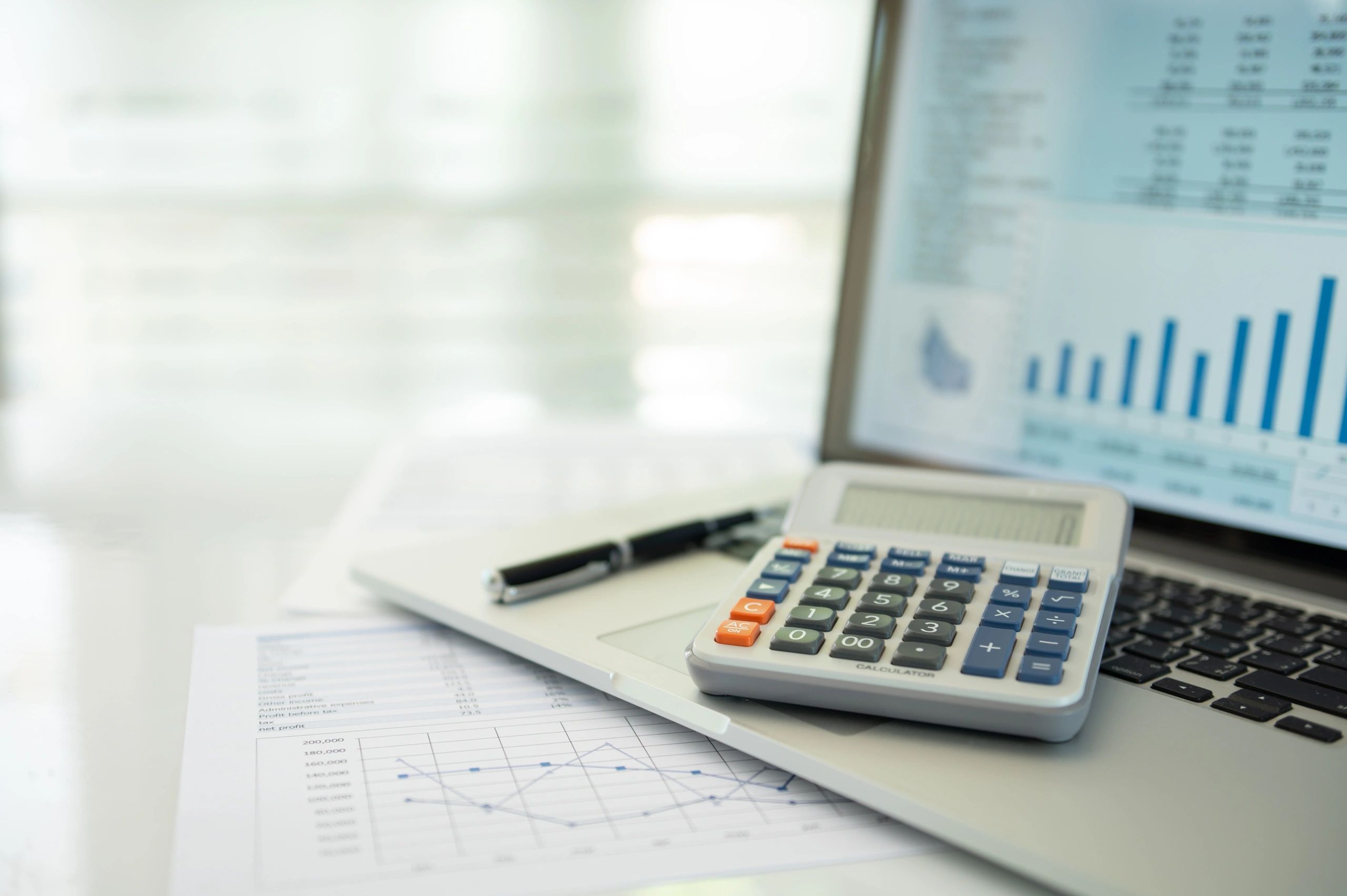 Small business owner reviewing numbers on a laptop with a calculator and financial reports